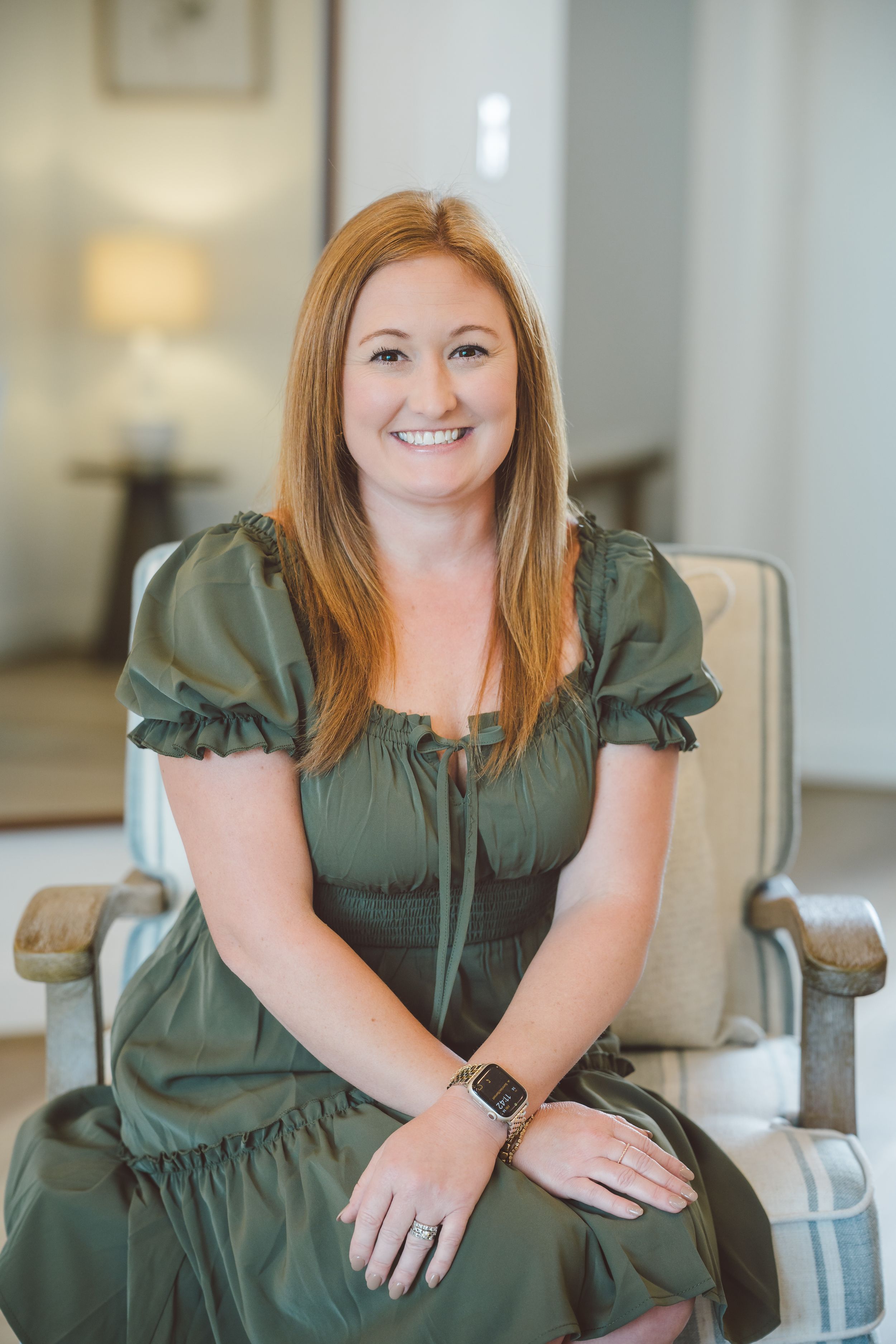 Professional portrait series showing someone in a green dress seated on a grey chair in a bright interior setting.