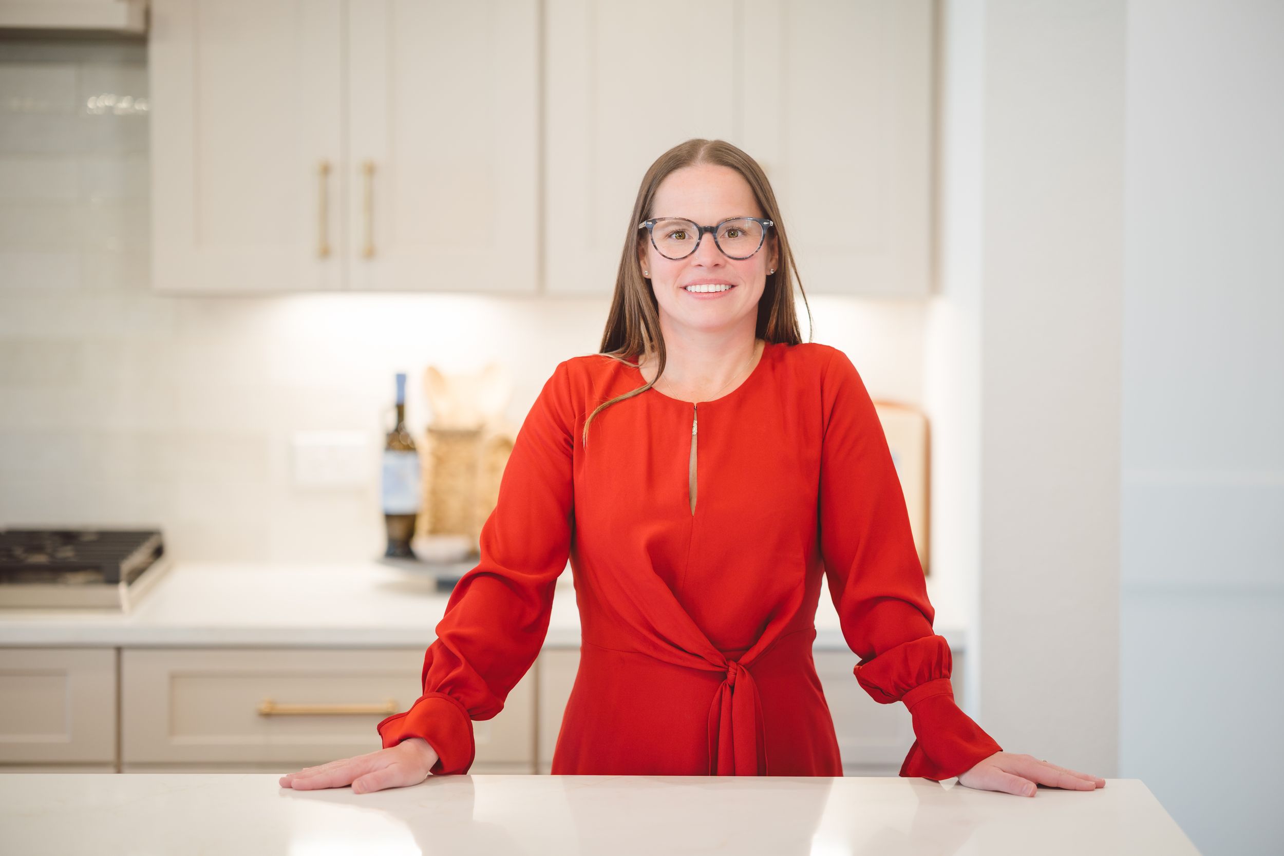 Someone wearing a bright red dress stands confidently in a modern white kitchen with quartz countertops.