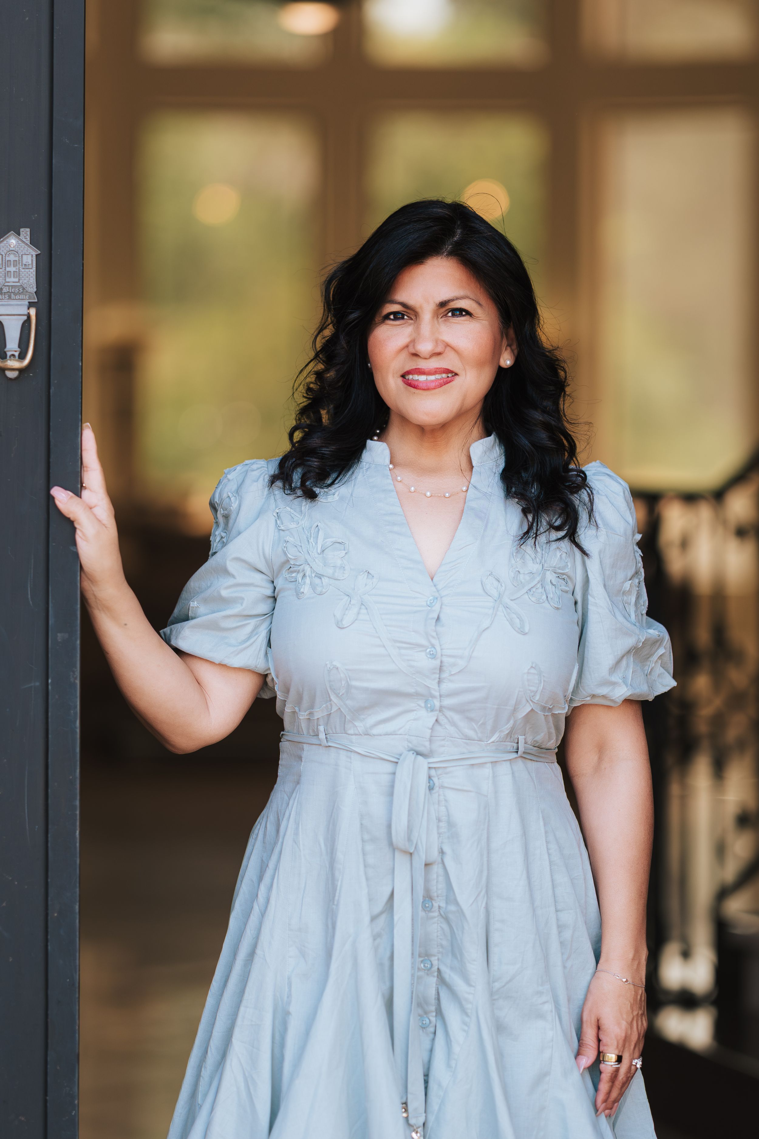 Woman in light blue dress smiling at doorway.