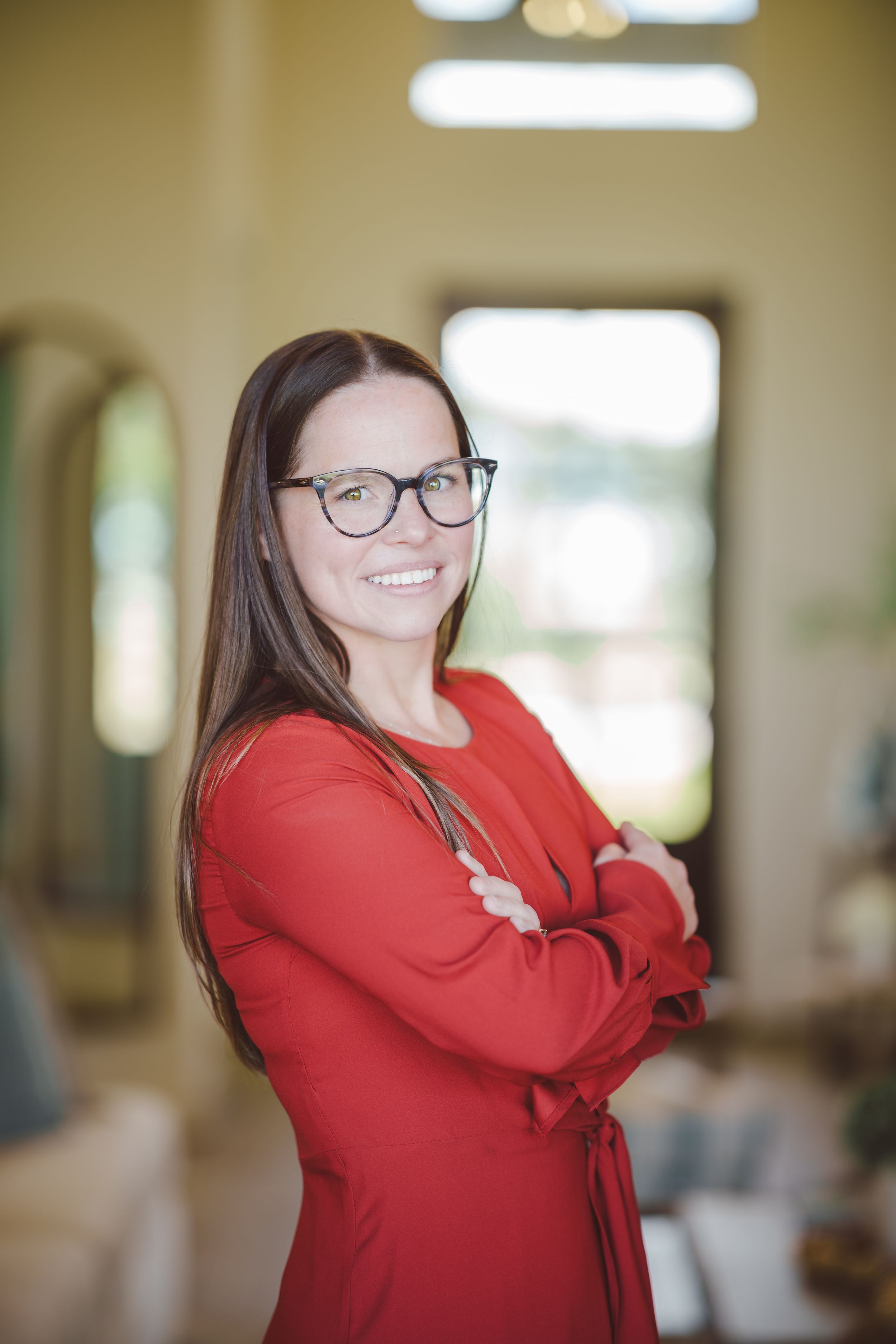 Person in a bright red sweater smiles and poses against a soft blurred background in an indoor setting.