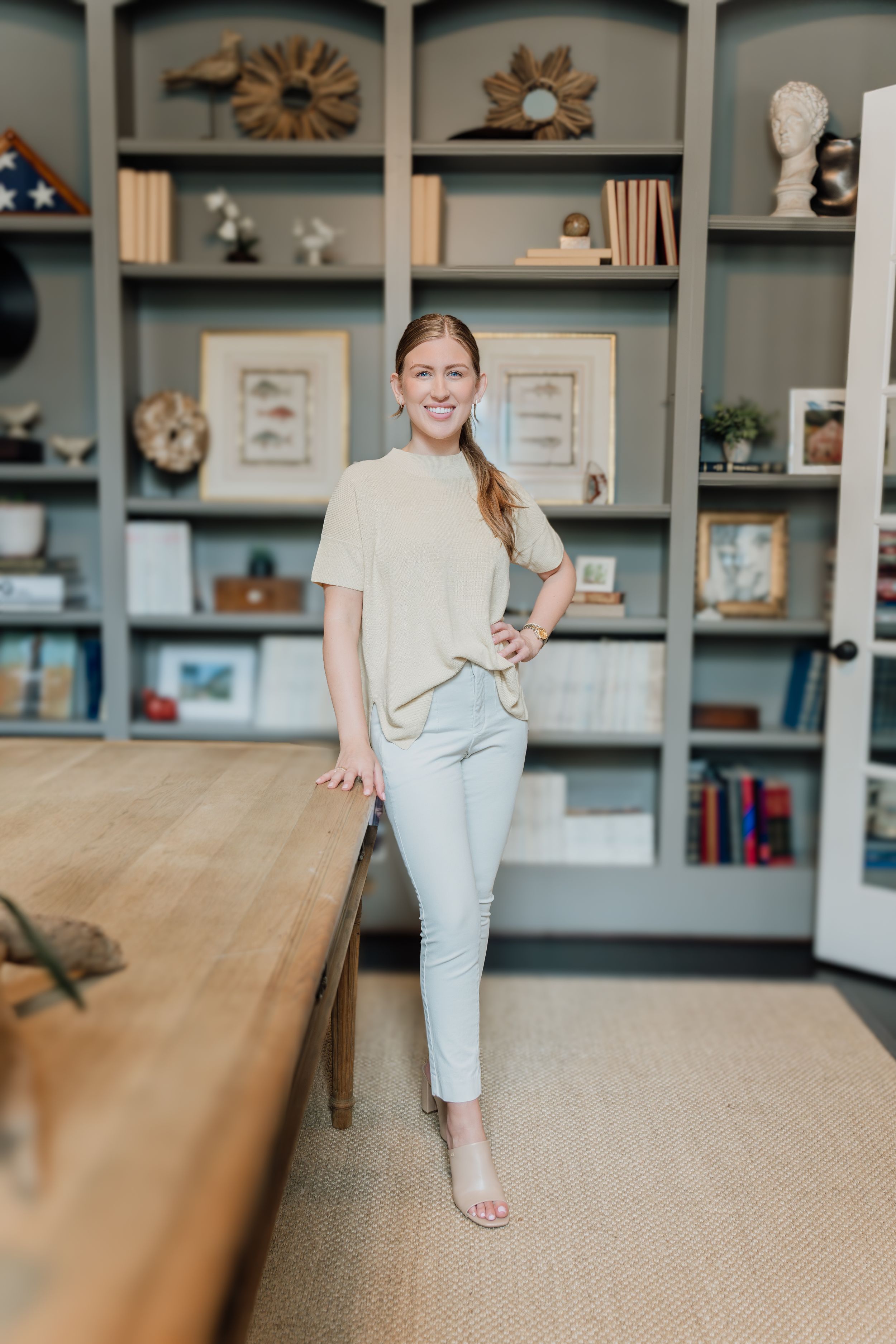 Woman in sage outfit posing confidently in a stylish home office with built-in shelving and wooden desk.
