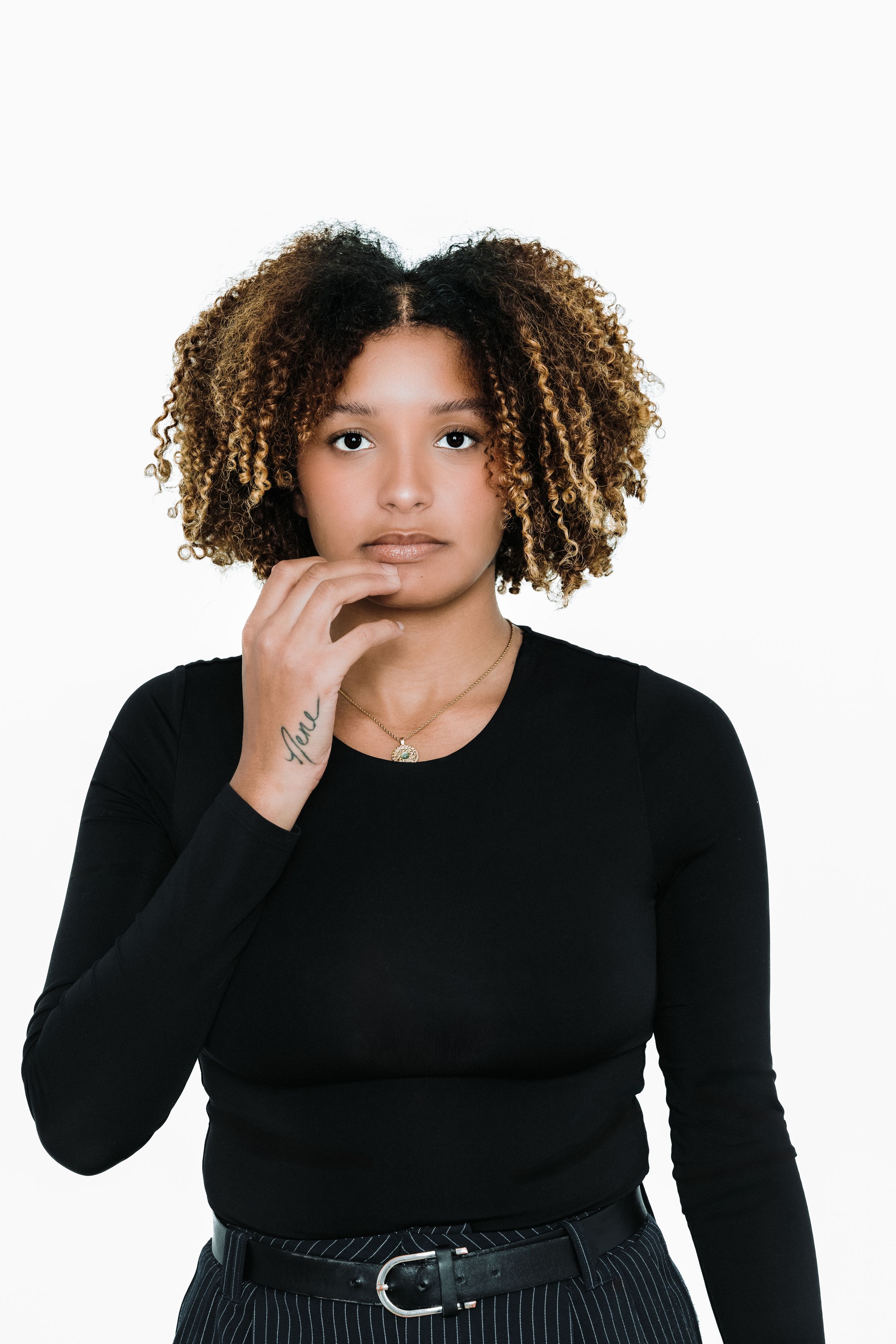 A person in a black long sleeve top poses playfully against a white background while making silly gestures.