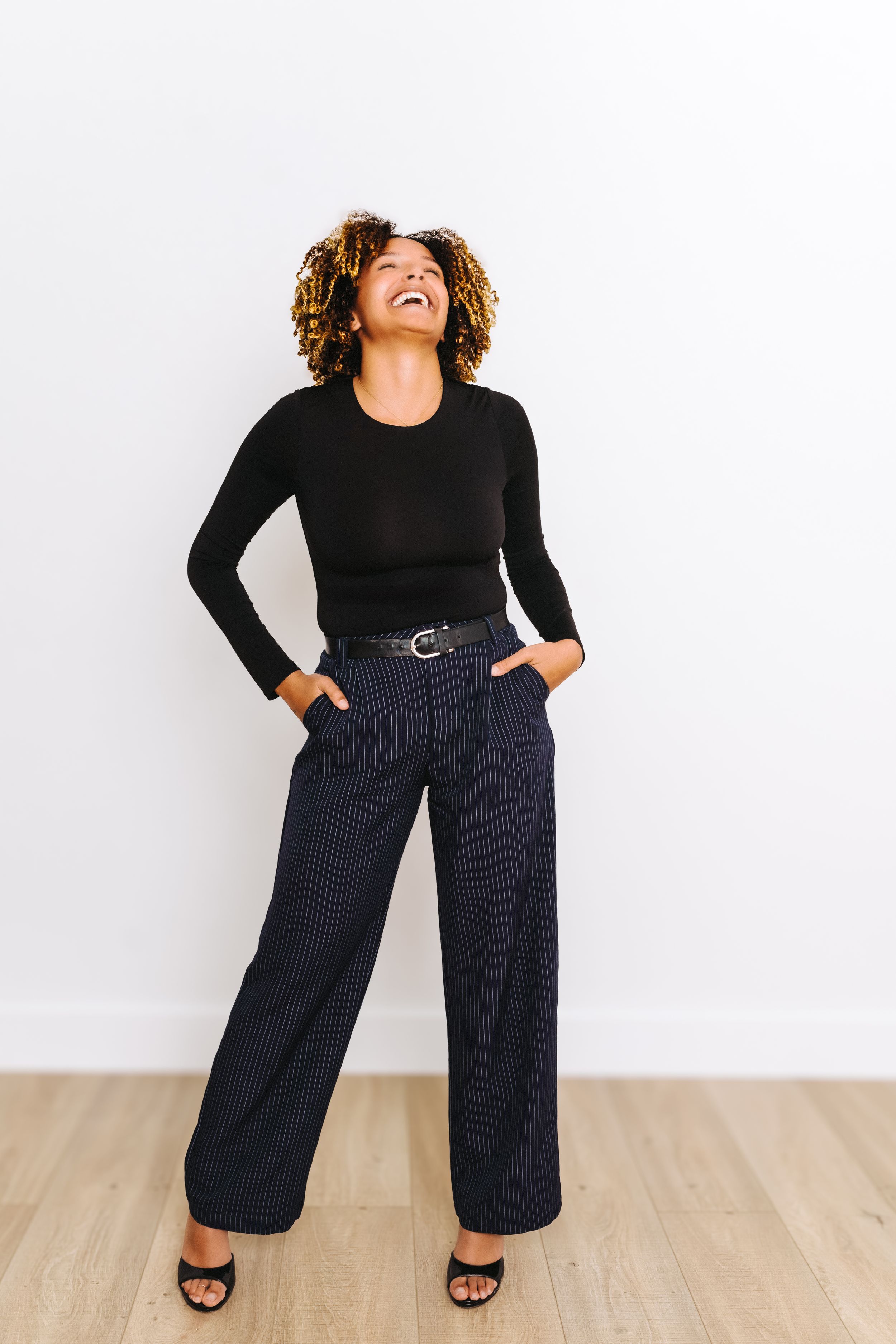 Four views of a model wearing a black long sleeve top with navy pinstripe wide leg pants and sandals on a light background.