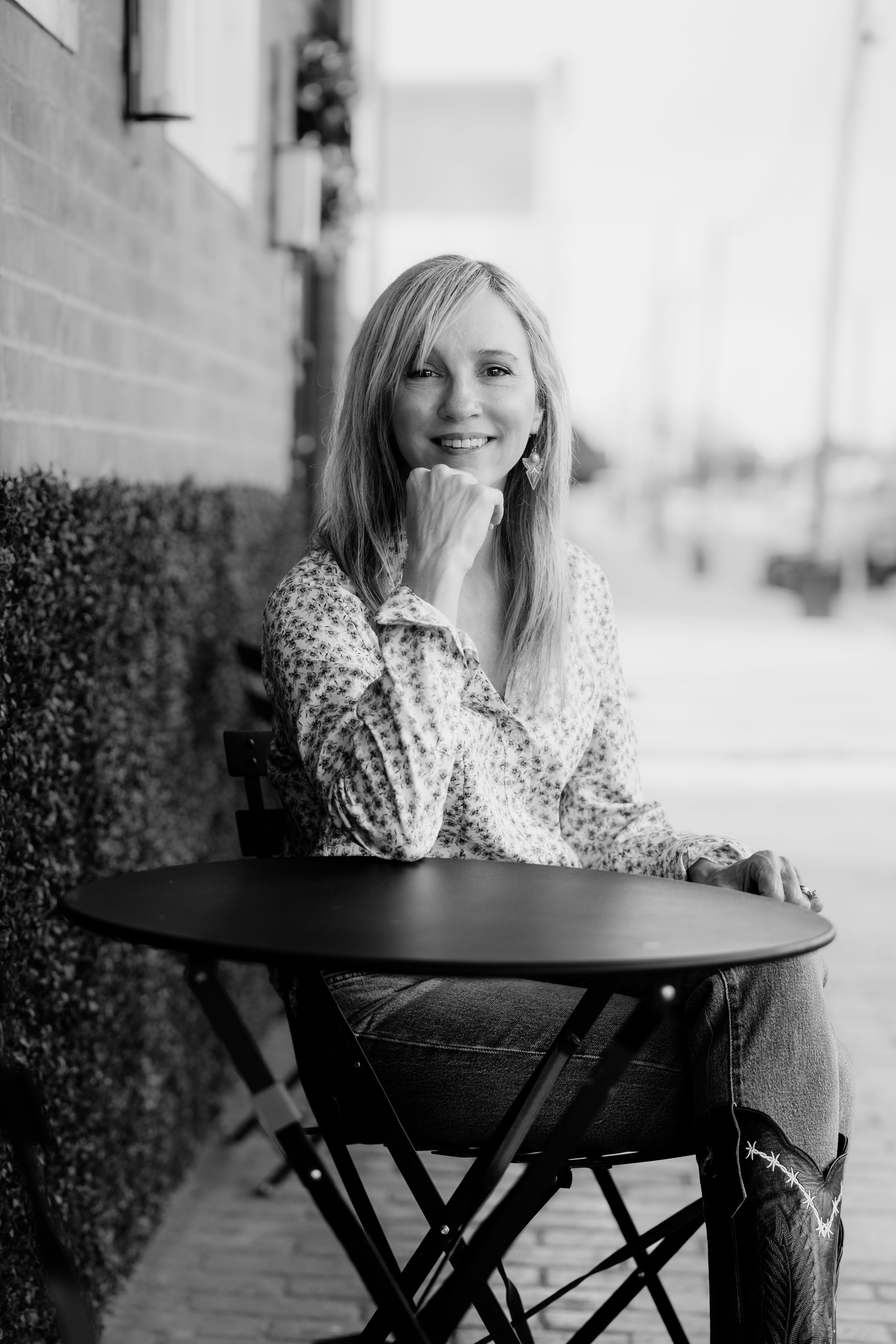 Black and white photo series of someone in a polka dot top and jeans posing casually at a small round table outdoors.