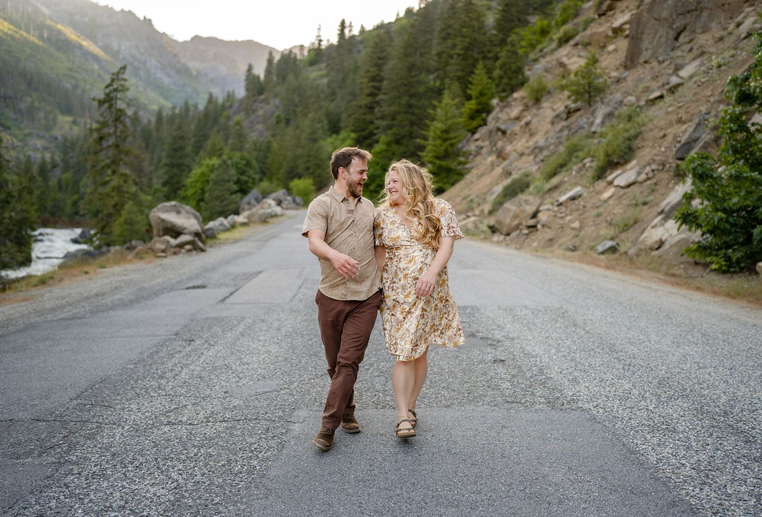 A couple walks together on a mountain road with scenic peaks in the background.