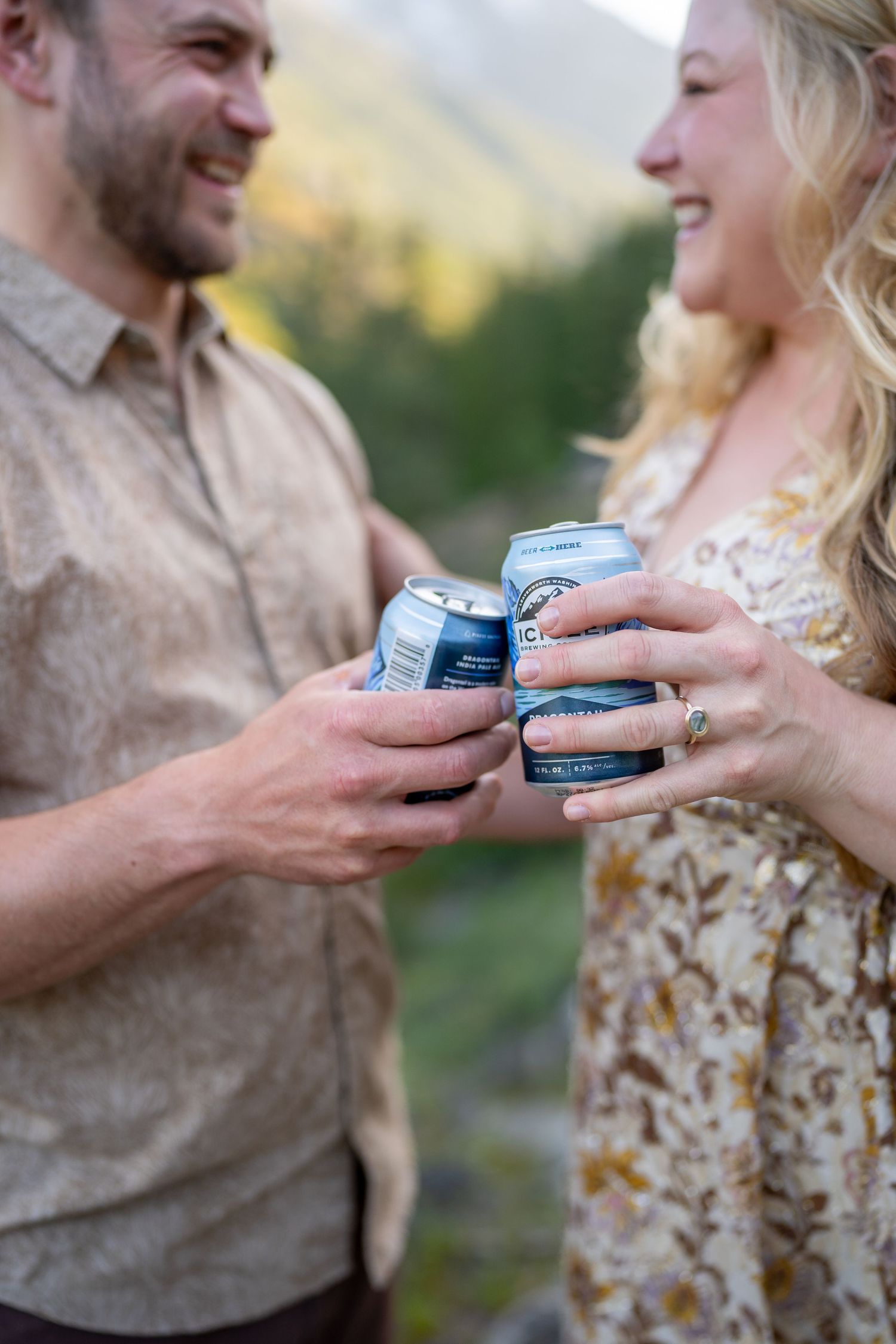 A couple shares drinks and laughter in a mountain setting during golden hour.