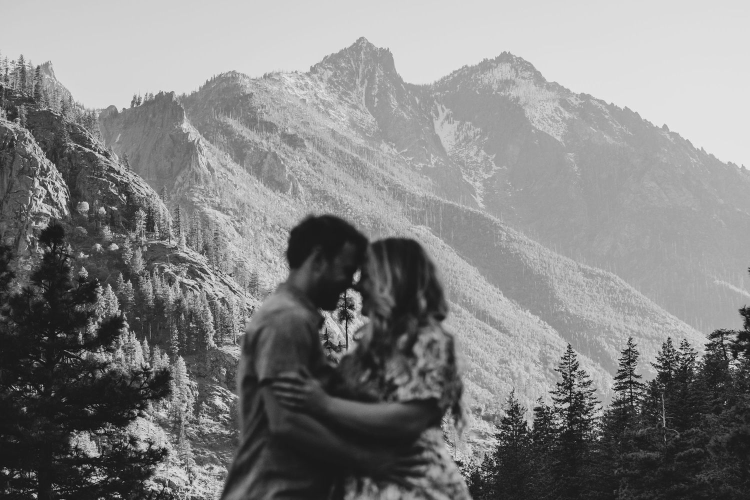 A silhouetted couple embraces against a dramatic mountain backdrop in black and white.