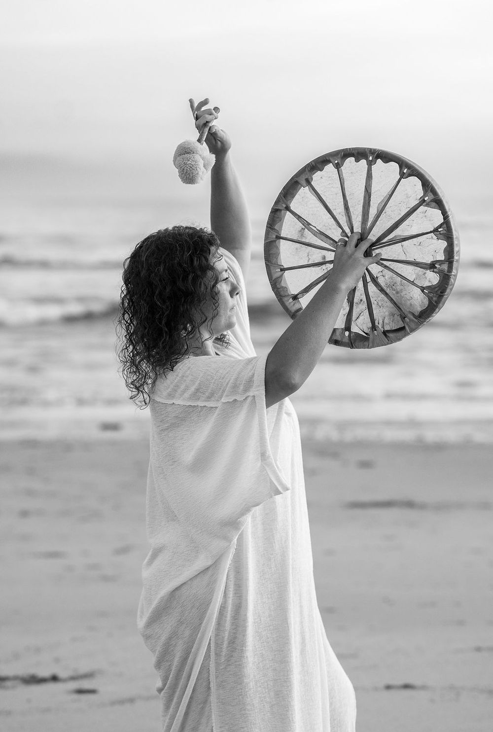 Black and white photo of a spiritual ceremony with drum and sage bundle against ocean backdrop.