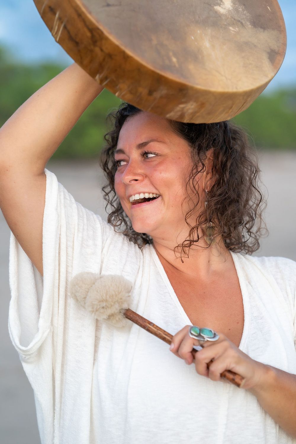Traditional wooden drum ceremony on beach with turquoise jewelry and white ceremonial dress.