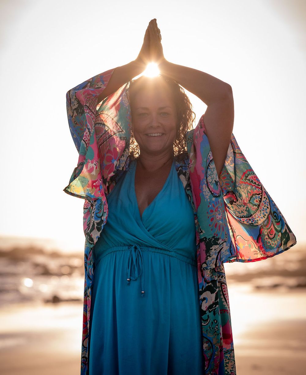 Sunlit beach portrait with arms raised wearing vibrant patterned kimono.