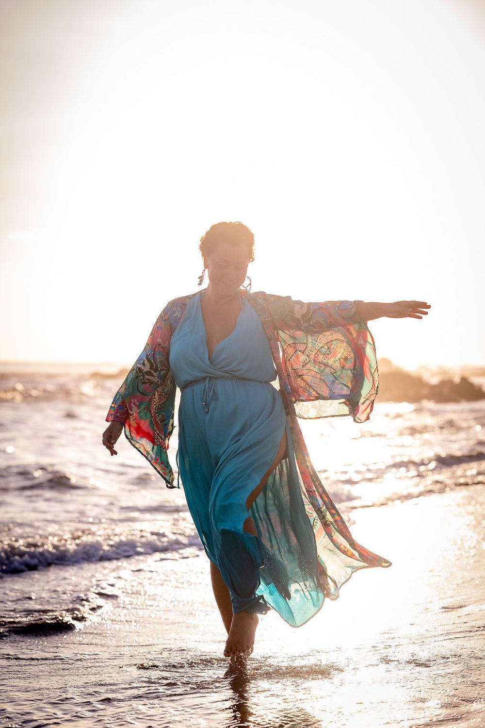 A figure in a flowing blue dress dances along the beach at sunset, creating a dreamy silhouette.