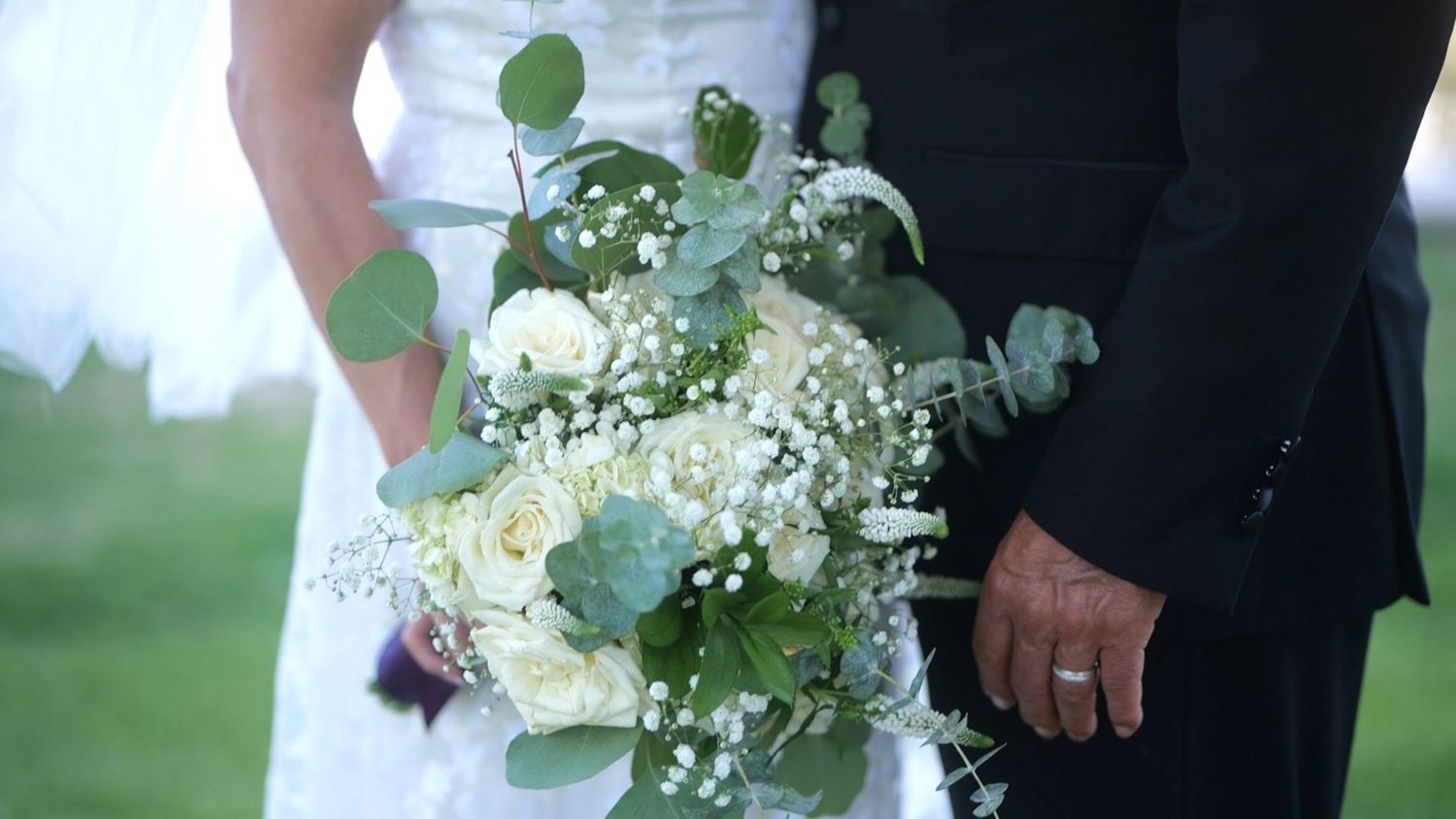 Elegant wedding bouquet featuring white roses and baby's breath held between bride and groom.