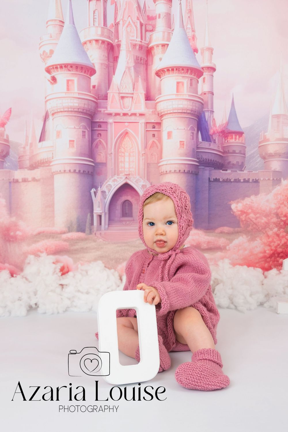 A pink-themed baby photo session with a magical fairytale castle backdrop and soft white clouds on the studio floor.