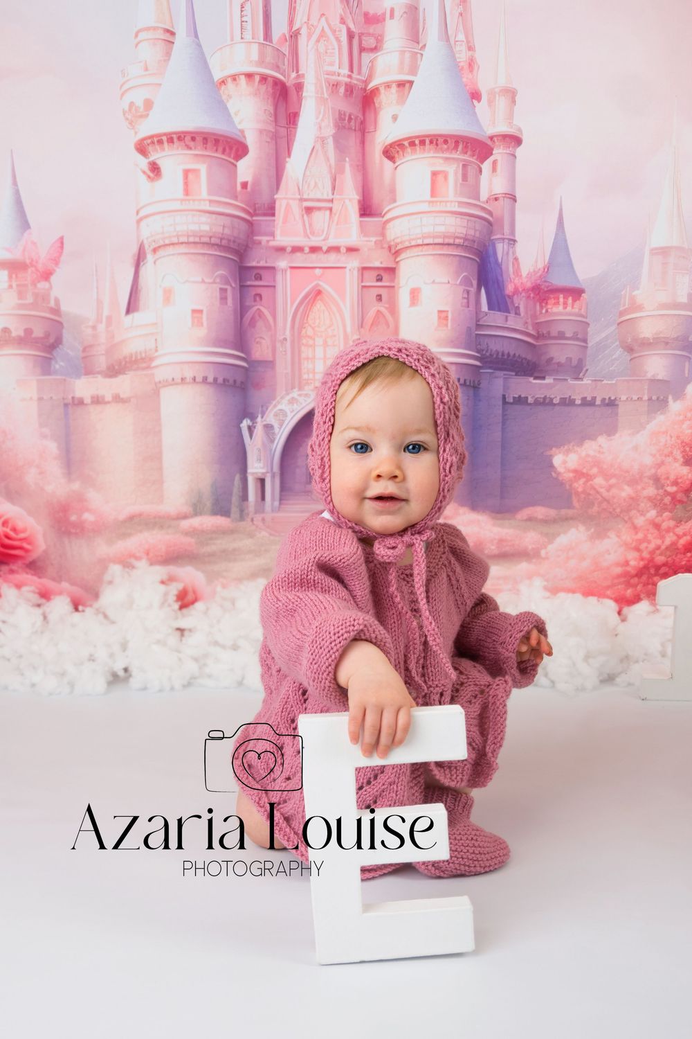 Professional portrait photo of a baby wearing a pink knitted outfit against a dreamy pink castle backdrop.