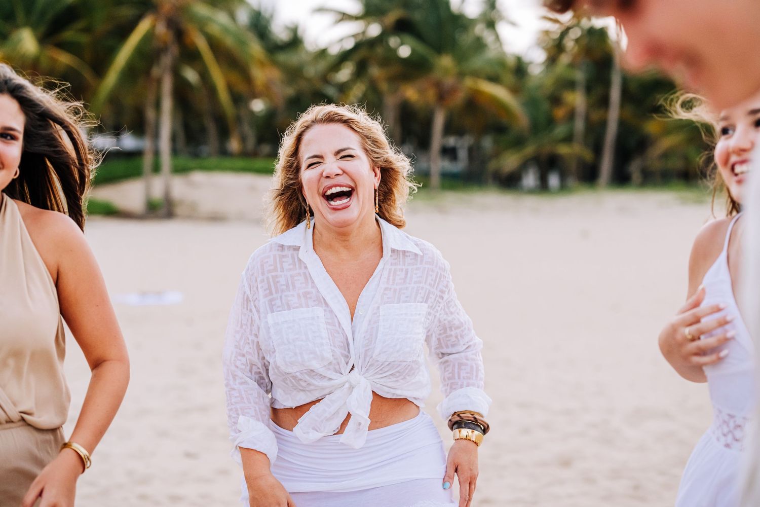 Candid moment of people laughing on tropical beach in white summer attire.