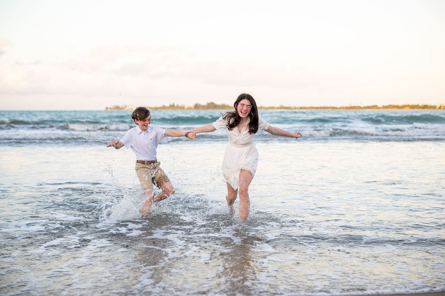 Two people splashing and playing in ocean waves at sunset.