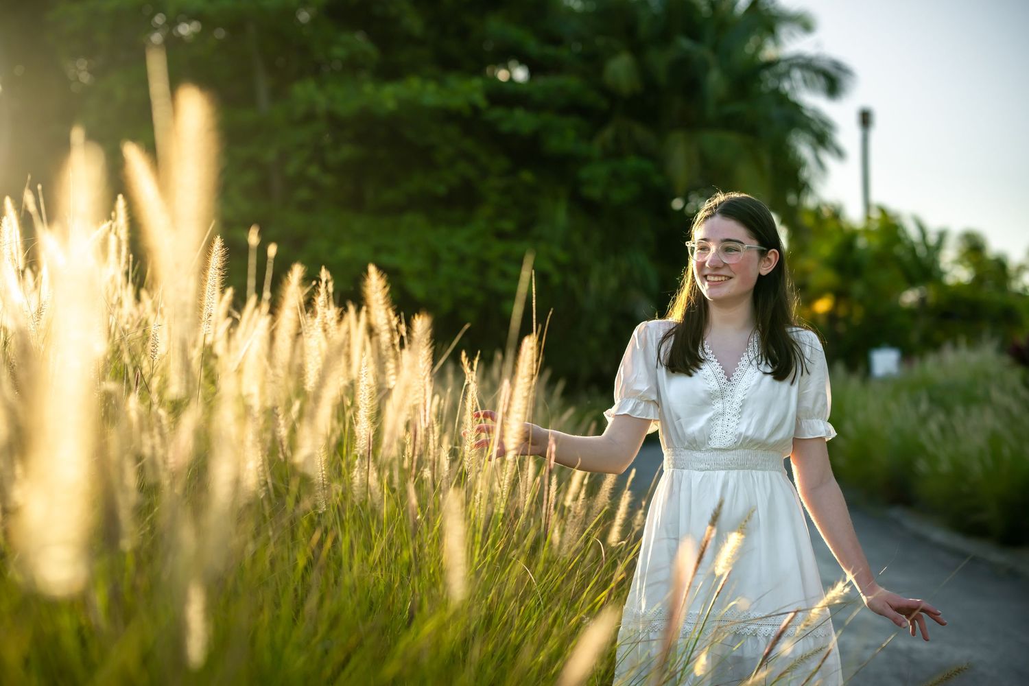 Young woman in white dress twirls through tall grass at sunset with soft golden lighting.