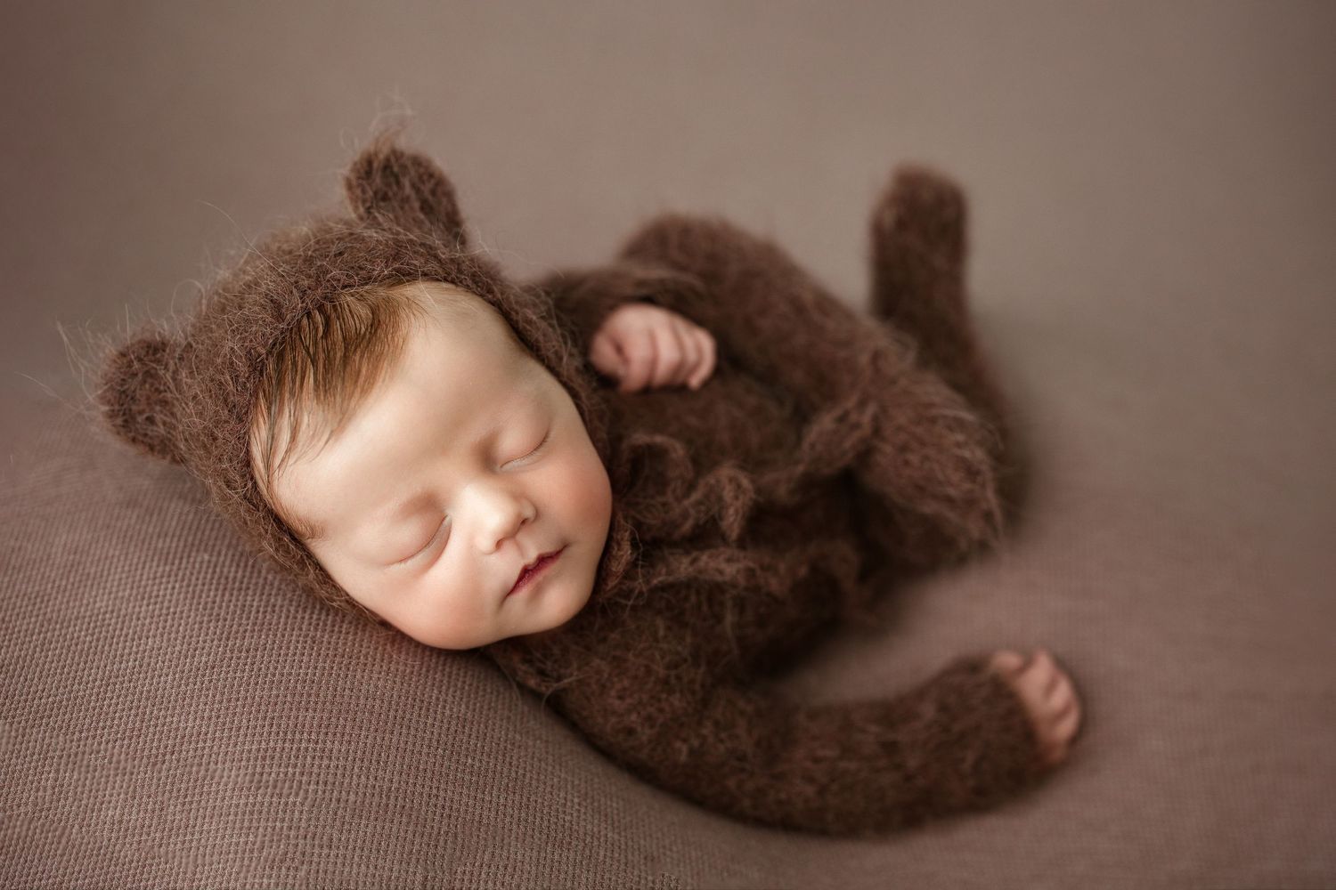 Newborn photography of sleeping baby wearing brown knit bear outfit on brown backdrop. Middle TN Newborn Photographer.