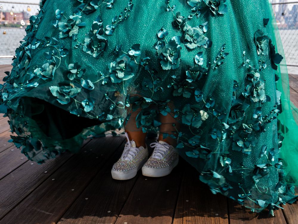 Close-up of sparkly sneakers peeking out under an emerald green formal dress with floral details.