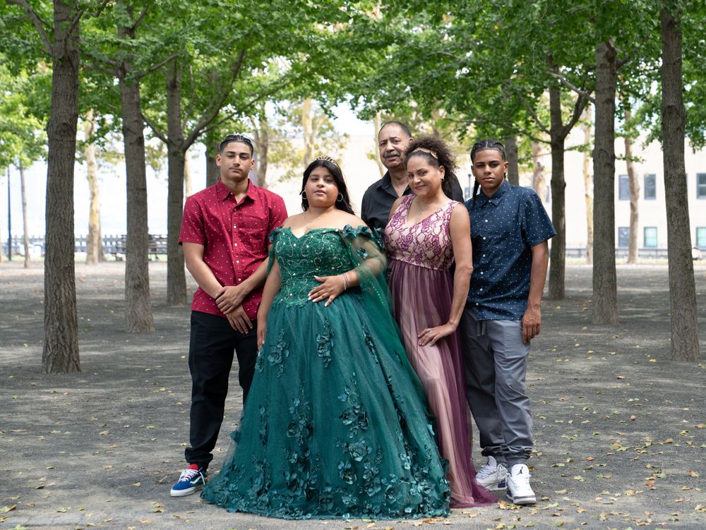 A group photo in a tree-lined park featuring formal attire and an emerald green ball gown.