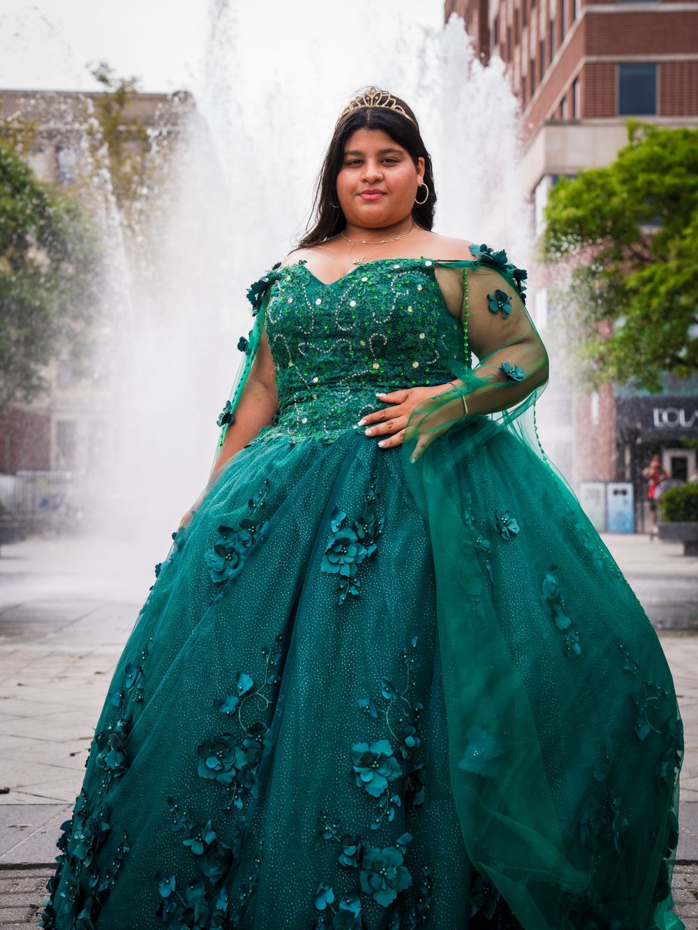 An emerald green ball gown with floral appliques photographed in front of a fountain.