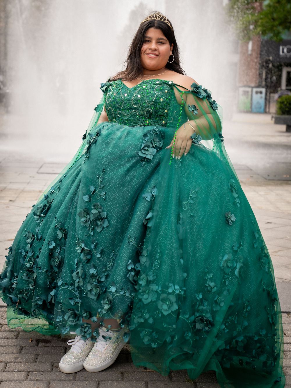 A stunning emerald green ball gown with floral appliques paired with white sneakers in an outdoor setting.