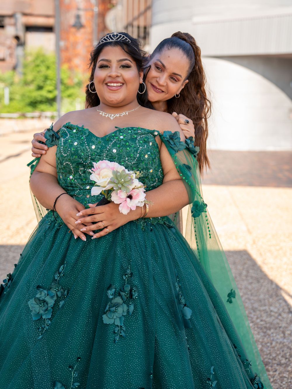 A formal emerald green gown with delicate floral details and a bouquet of pink flowers.