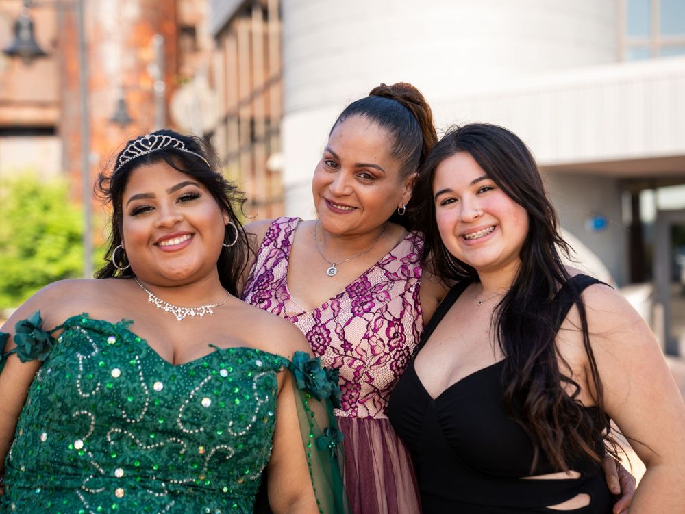 Three people smiling together at a formal event against a modern building backdrop.