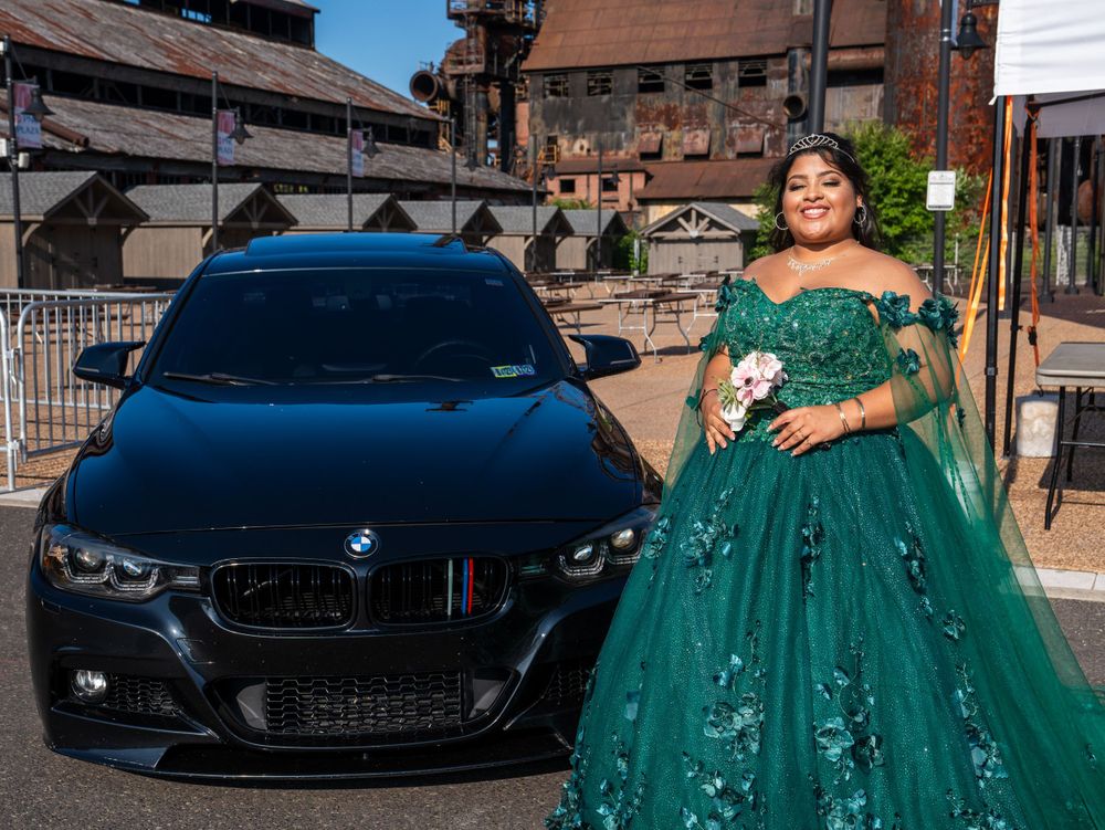 An emerald green ball gown posed next to a black BMW in an urban setting.