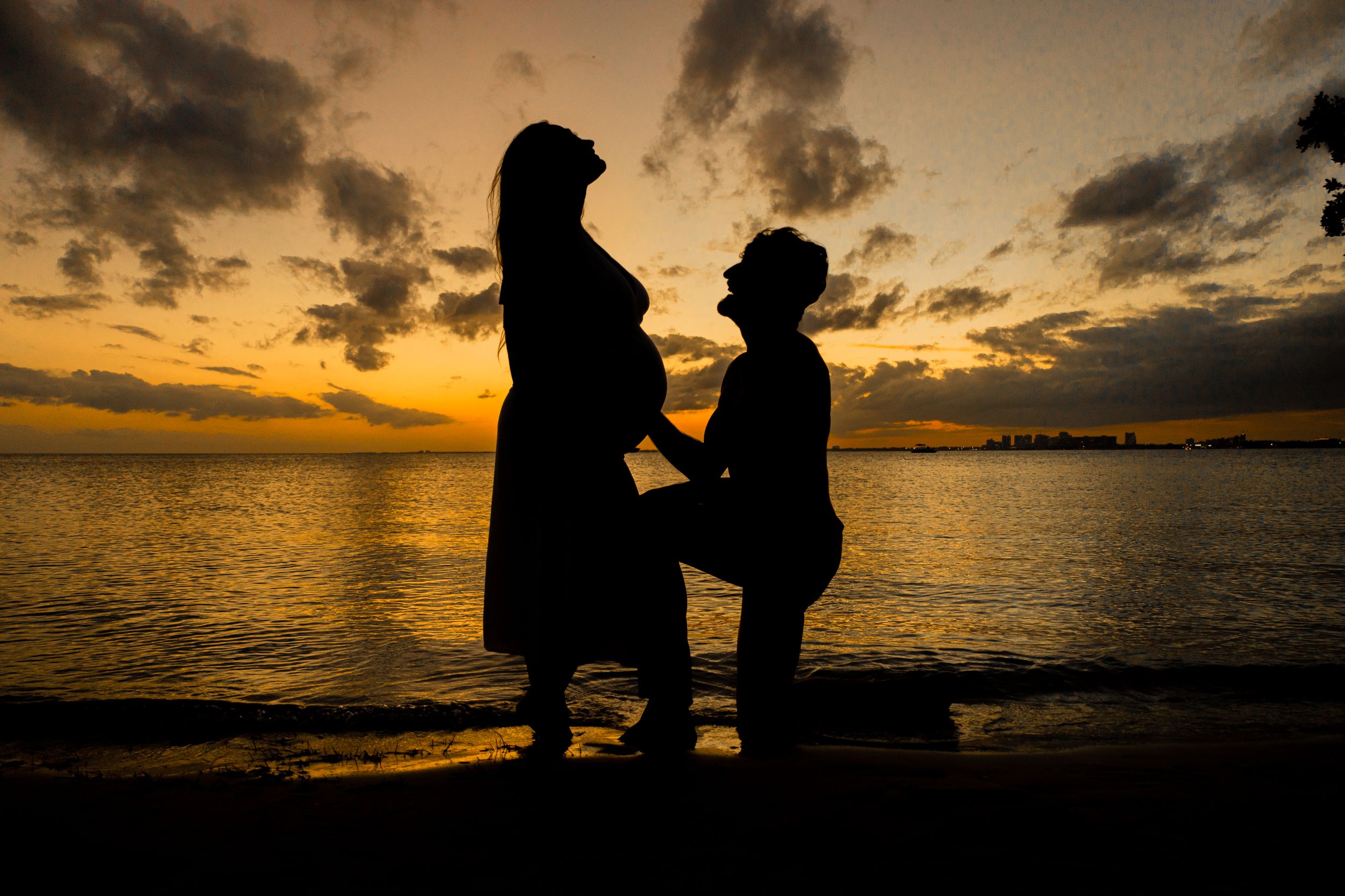 Silhouetted couple sharing intimate moment on beach during sunset proposal.