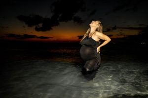 Silhouette of an expectant mother posing in water during golden hour sunset.