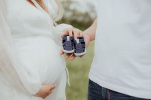 Close-up of tiny baby shoes held against pregnant belly.