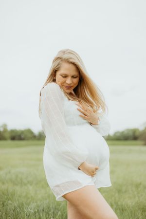 Expectant mother in white dress twirling joyfully in field.