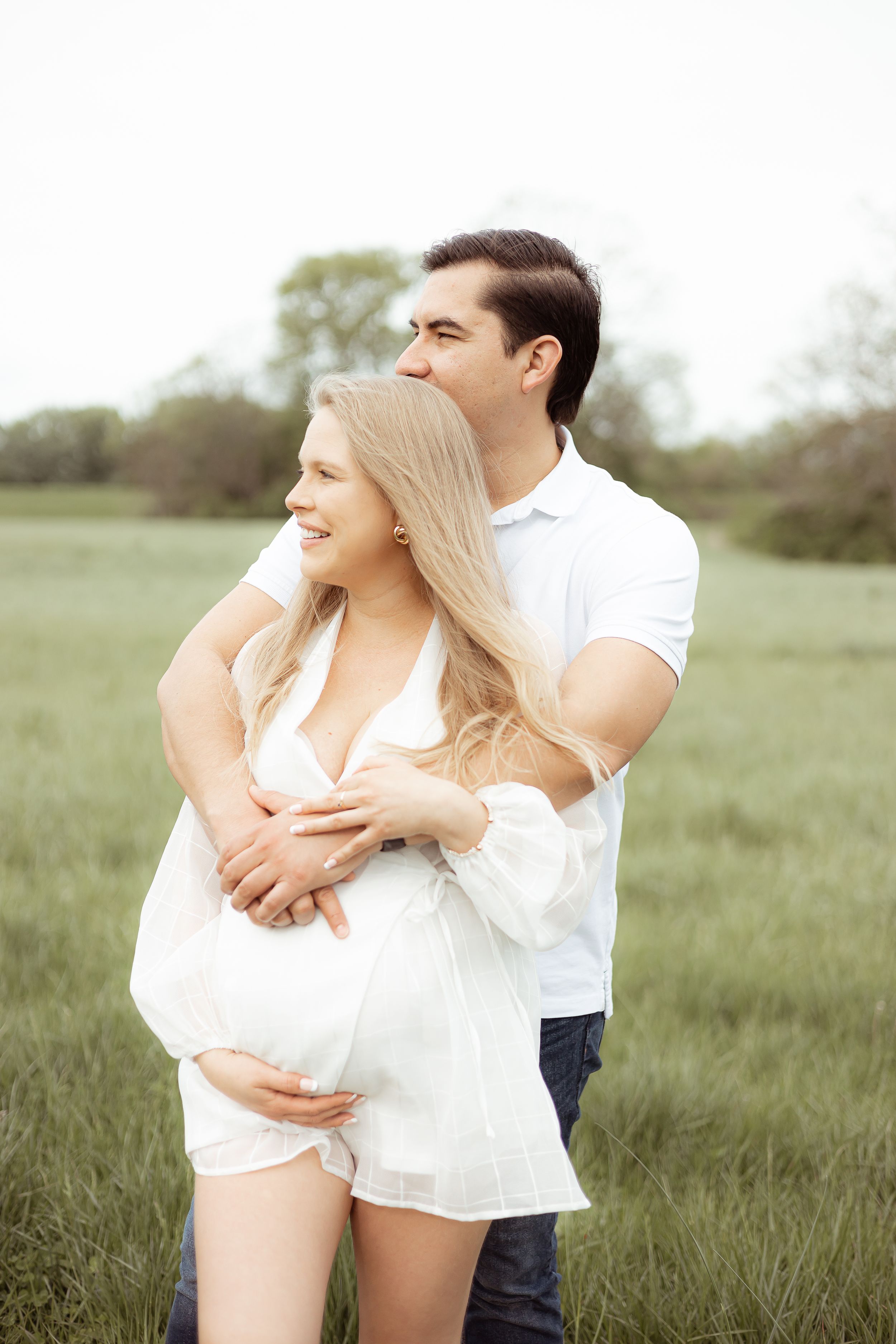 Couple sharing intimate moment in grassy field during maternity photoshoot.