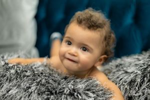 Baby lying on soft gray furry blanket with bright blue background.