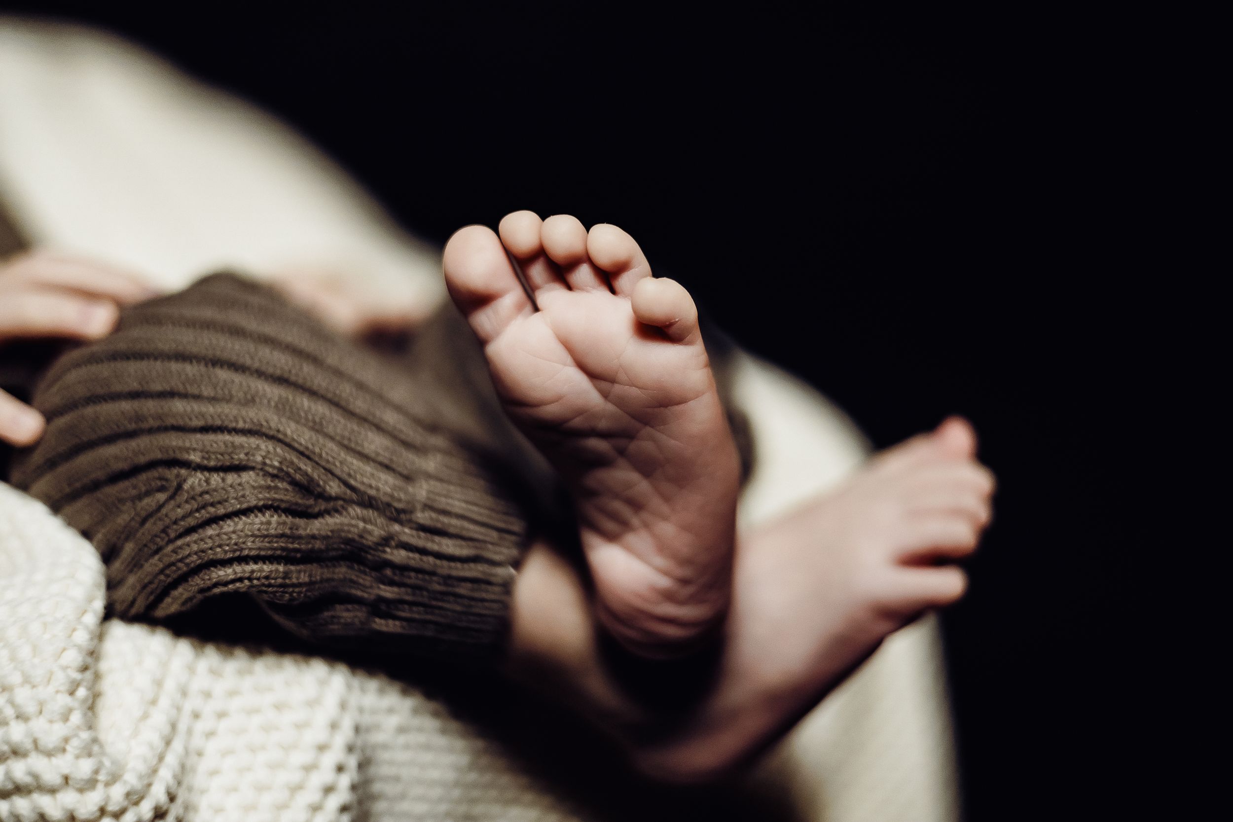 Close-up of tiny baby feet resting on knitted brown and white blankets.