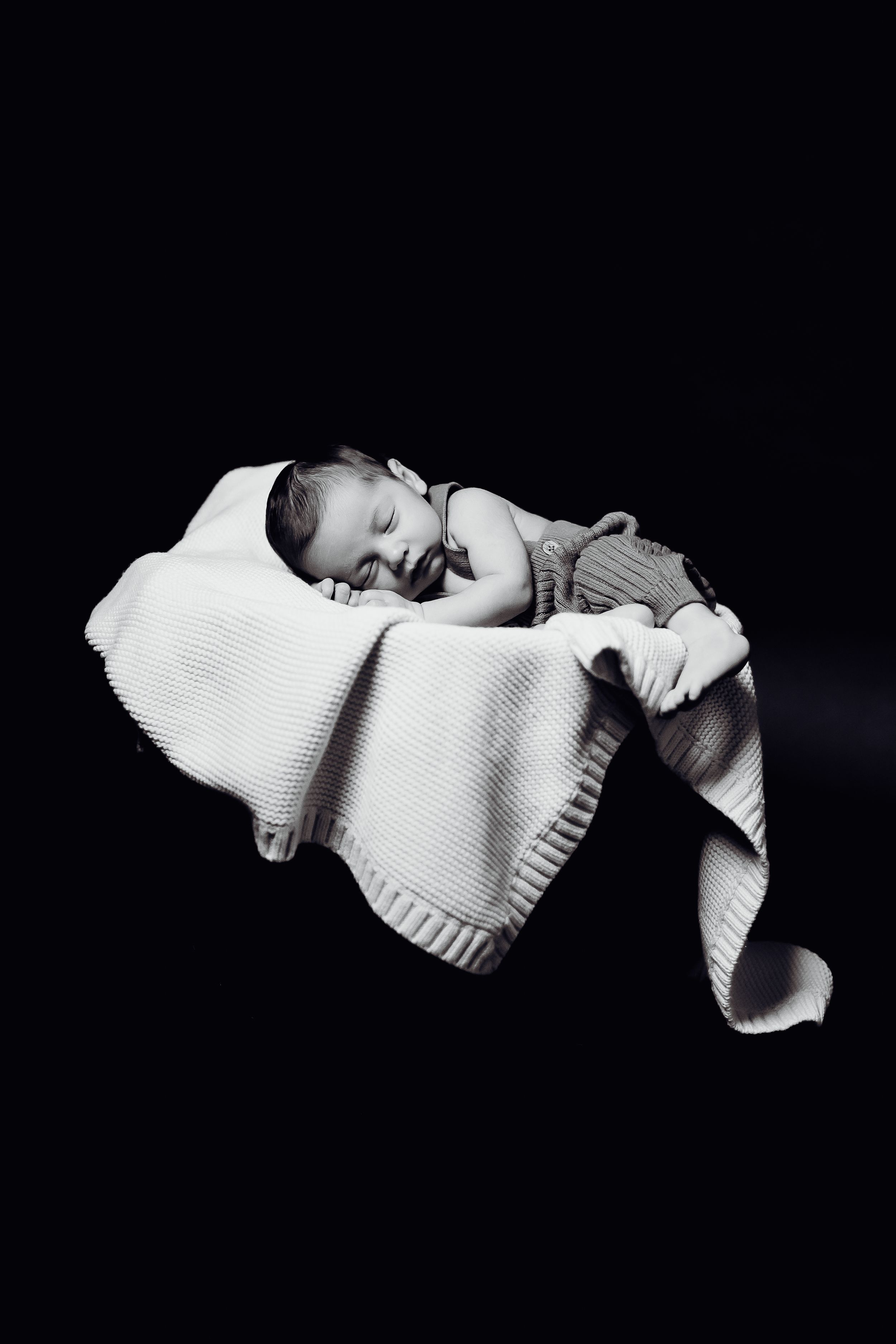 Baby sleeping peacefully on white knitted blanket in black and white portrait.