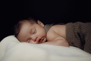 Peaceful newborn baby sleeping on soft white blanket against black background.