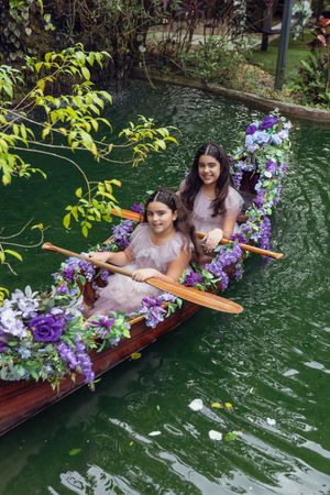 Purple and white flower decorated rowboat with passengers floating on green water.