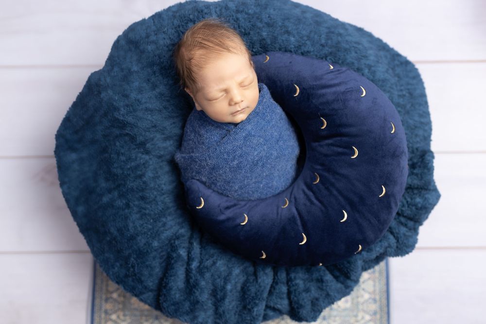 Sleeping baby on navy blue cushion with moon pattern against blue background.
