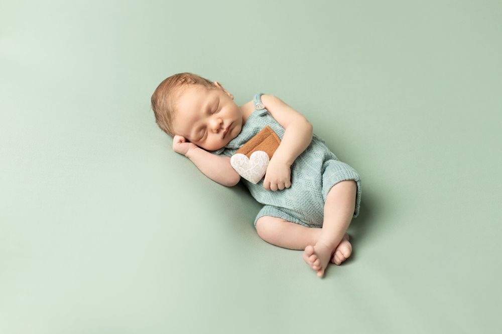 Newborn baby wearing light blue outfit lying on mint green background smiling during professional photo session.