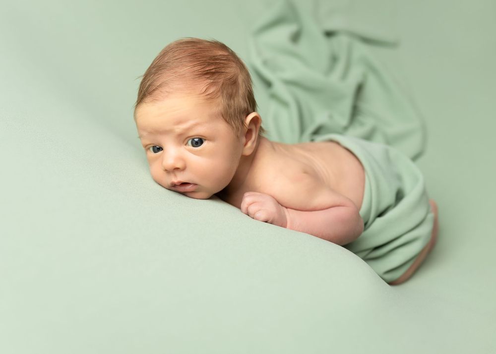 Baby lying on soft mint green fabric during professional newborn photography session.