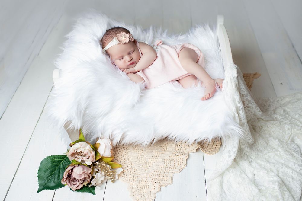 Newborn photography session with white fur and wooden floor backdrop.