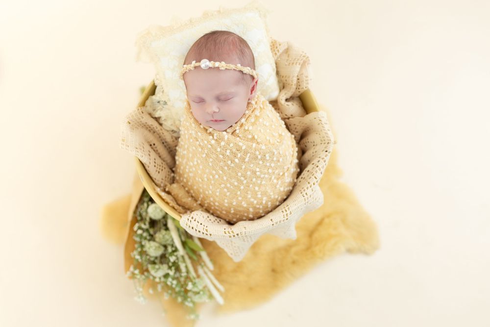 Sleeping newborn wrapped in cream blanket with floral accents during professional photo session.