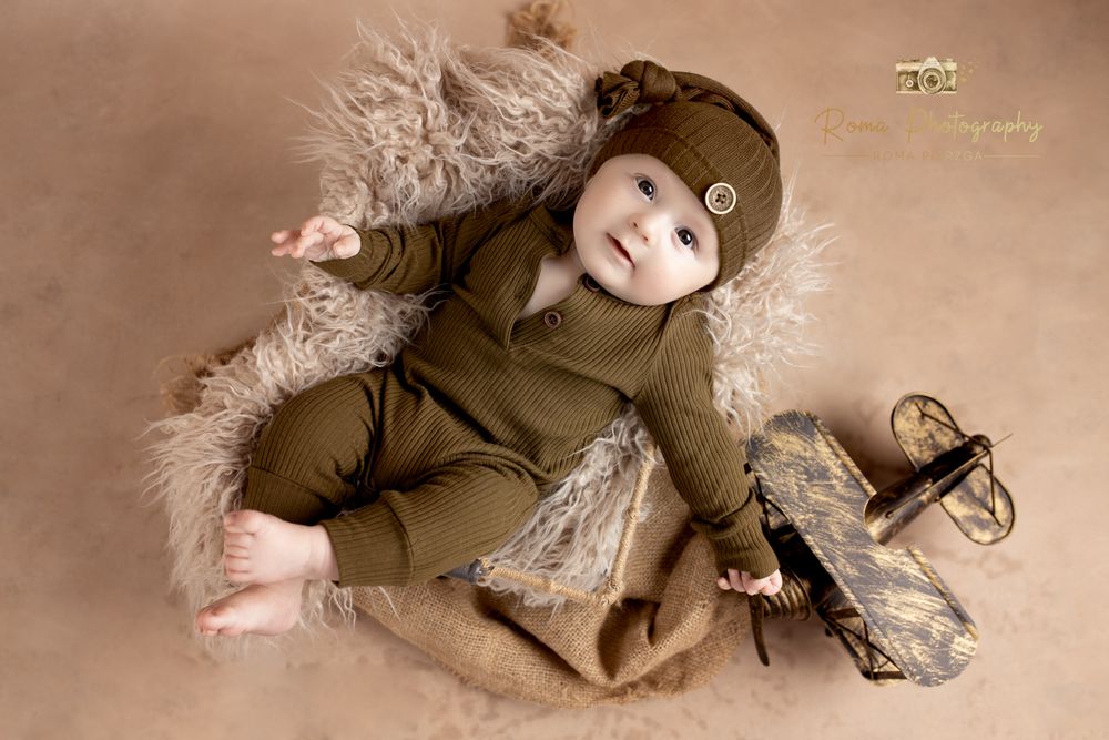 Baby dressed in brown outfit lying on furry backdrop with vintage props.