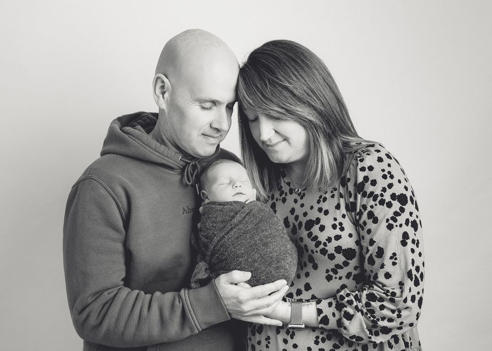 Black and white family portrait showing tender moment with newborn.