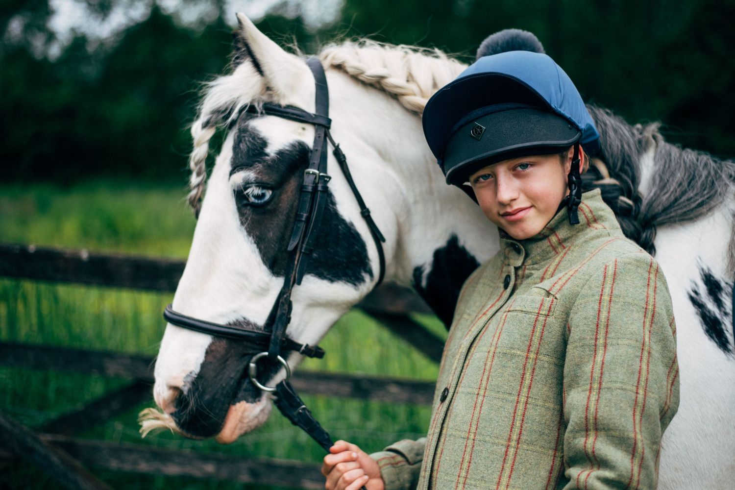 A black and white horse with riding tack stands next to someone in equestrian gear.