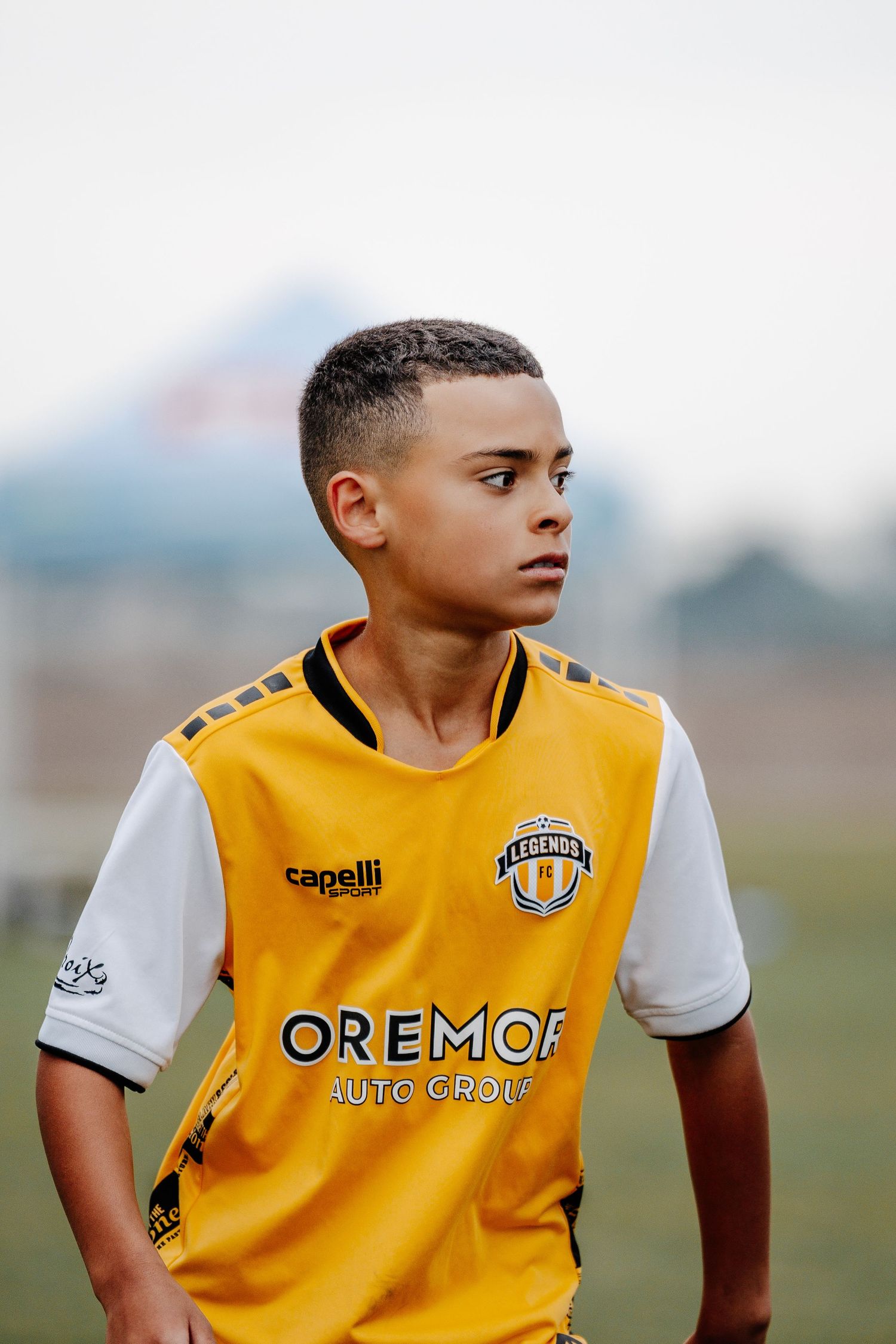 Soccer player wearing yellow and white Legends FC jersey stands on sports field.