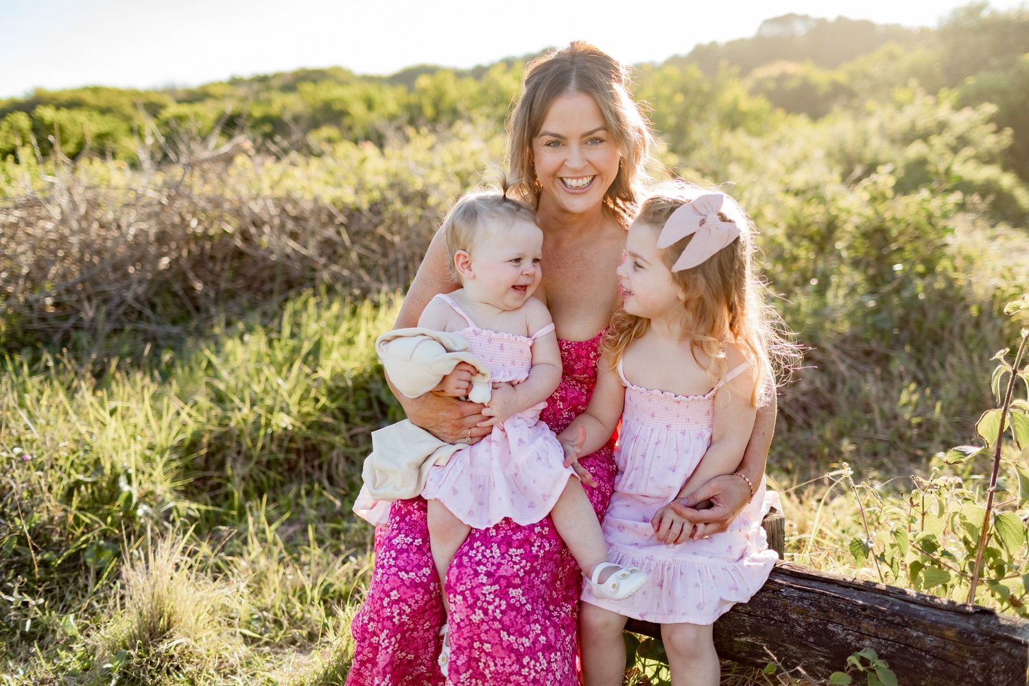 Family shares loving moment while sitting together outdoors in coordinated pink outfits.