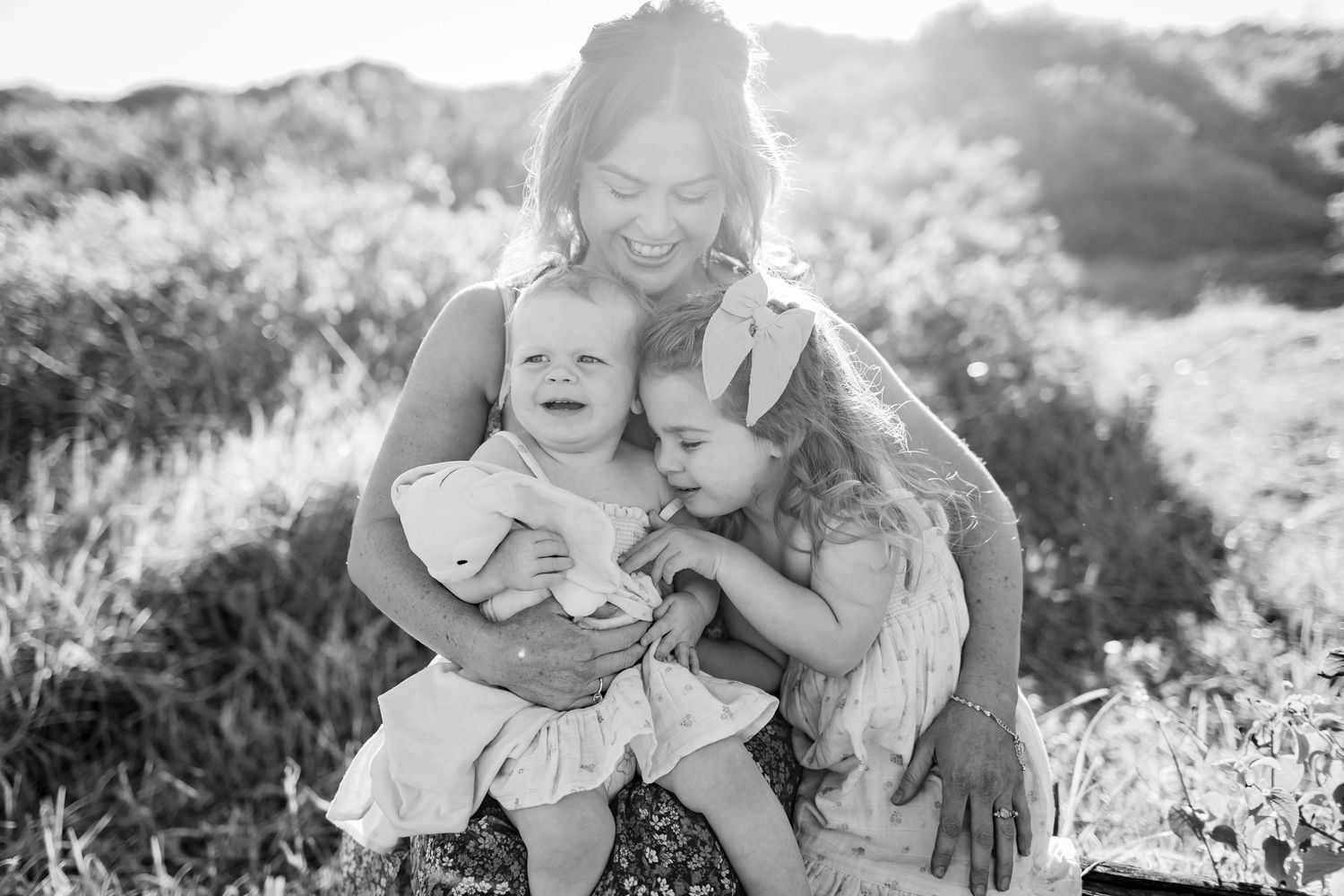 Black and white portrait of three people embracing outdoors in natural setting.
